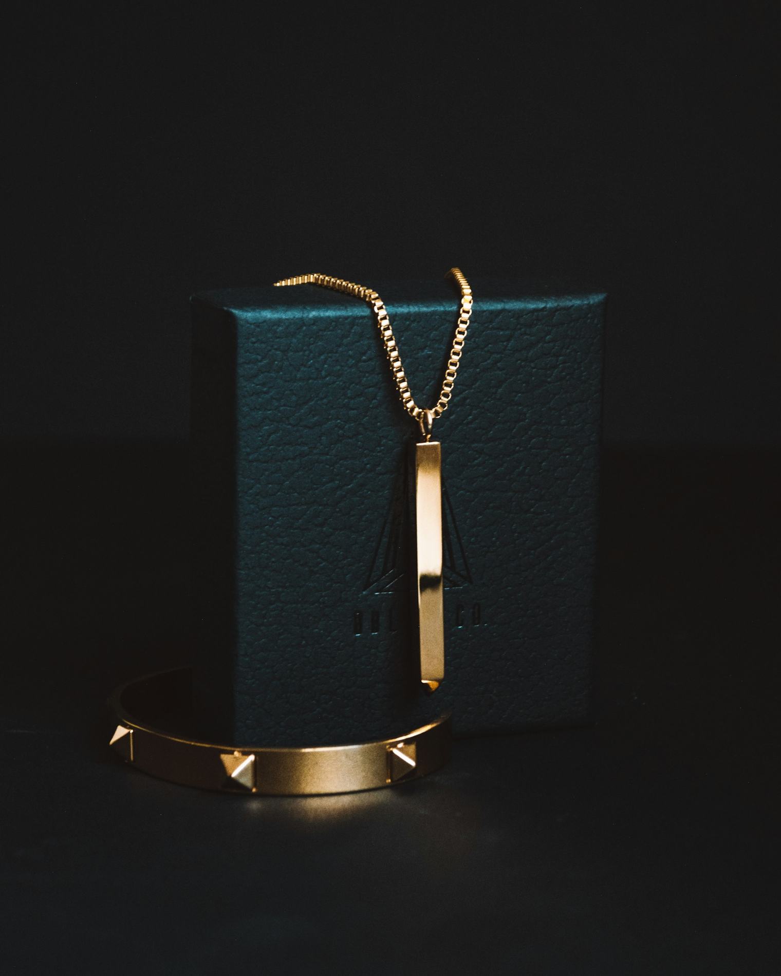 A gold chain and bar pendant on a dark leather jewellery box