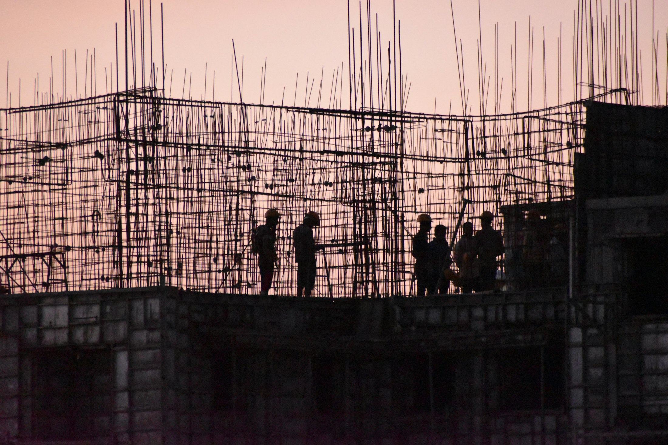 Construction workers silhouetted against rebar at dusk